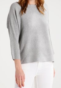 Grå ribbad tröja med lös passform, båthalsringning och trekvartslånga ärmar, tillsammans med vita byxor. Mjuk textur och enkel design.