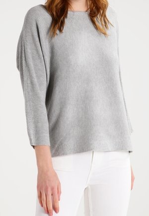 Maglione grigio a coste con una vestibilità ampia, collo a barca e maniche a tre quarti, abbinato a pantaloni bianchi. Texture morbida e design semplice.