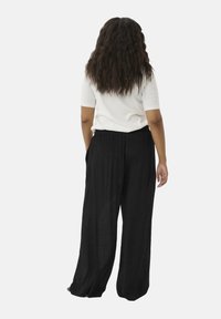Pantalones anchos negros hechos de una tela ligera con un acabado texturizado, con una cinturilla elástica. El modelo se ve desde la espalda.