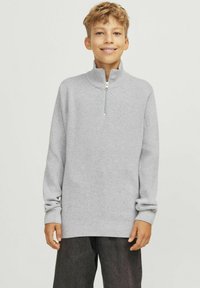 Pilkas zip-up megztinis su aukštu apykakle ir ilgomis rankovėmis. Pagamintas iš minkštos medžiagos, pasižymi laisvu siluetu ir tekstūra su gumbais.