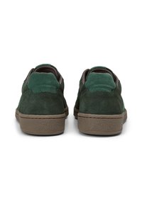 Grüne Wildledersneaker mit einer strukturierten braunen Gummisohle und kontrastierenden grünen Akzenten an der Ferse und der Zunge. Die Rückansicht zeigt genähte Details.