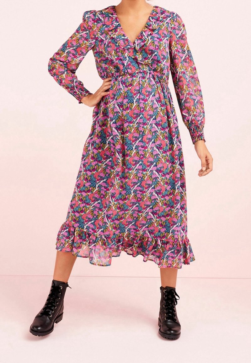 Femme portant une robe midi rose à fleurs avec un ourlet à volants et des manches longues, associée à des bottines noires à lacets.
