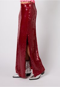 Czerwona spódnica z cekinami, z bocznym rozcięciem, dopasowanym krojem i błyszczącą fakturą. Połączona ze srebrnymi botkami za kostkę z zaostrzonym noskiem i niskim obcasem.