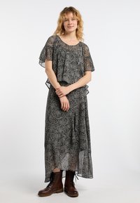 Černé a krémové maxi šaty s paisley vzorem, volnými rukávy, lehkým materiálem a asymetrickým lemem. Doplněné hnědými šněrovacími botami.