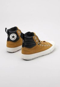 Zapatillas altas de ante marrón con acentos de cuero negro, suelas de goma blanca y logo plateado de Converse All Star en el talón.