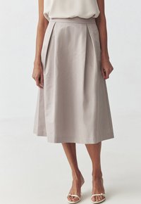 Jupe plissée grise pâle avec une texture lisse, de longueur genoux, dotée d'une taille et de poches latérales, associée à des sandales plates blanches.