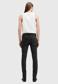 Schwarze Skinny Jeans mit hoher Taille, Gürtelschlaufen und zwei Gesäßtaschen. Kombiniert mit einem weißen ärmellosen Oberteil. Glatte Stoffstruktur.