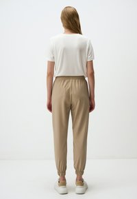 Beige relaxte broek met een elastische tailleband en boorden, gecombineerd met een eenvoudige witte T-shirt met korte mouwen en witte sneakers.
