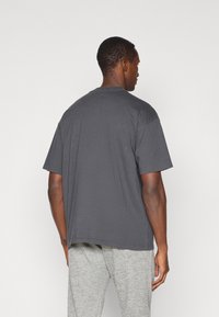 Grå t-skjorte med korte ermer som har rund hals og ledig passform, laget av mykt materiale med en jevn tekstur, vist fra baksiden.