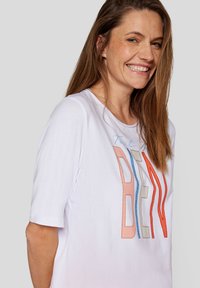 White short-sleeve t-shirt featuring colorful stitched text "Tout va bien" in orange, blue, and beige. Soft material, casual fit.