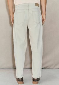 Lys beige denimjeans med straight fit, der har to baglommer, diskret syning og et mærke i taljen.