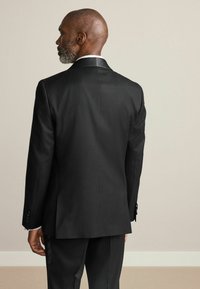 Black suit jacket with a smooth texture, single vent at the back, and shiny lapel. Displayed from the back. Tailored fit.