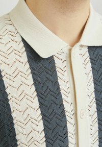 Maglietta polo in maglia con motivi a righe alternativi blu navy e crema. Presenta un design a zig zag testurizzato, chiusura a bottoni e colletto a costine.
