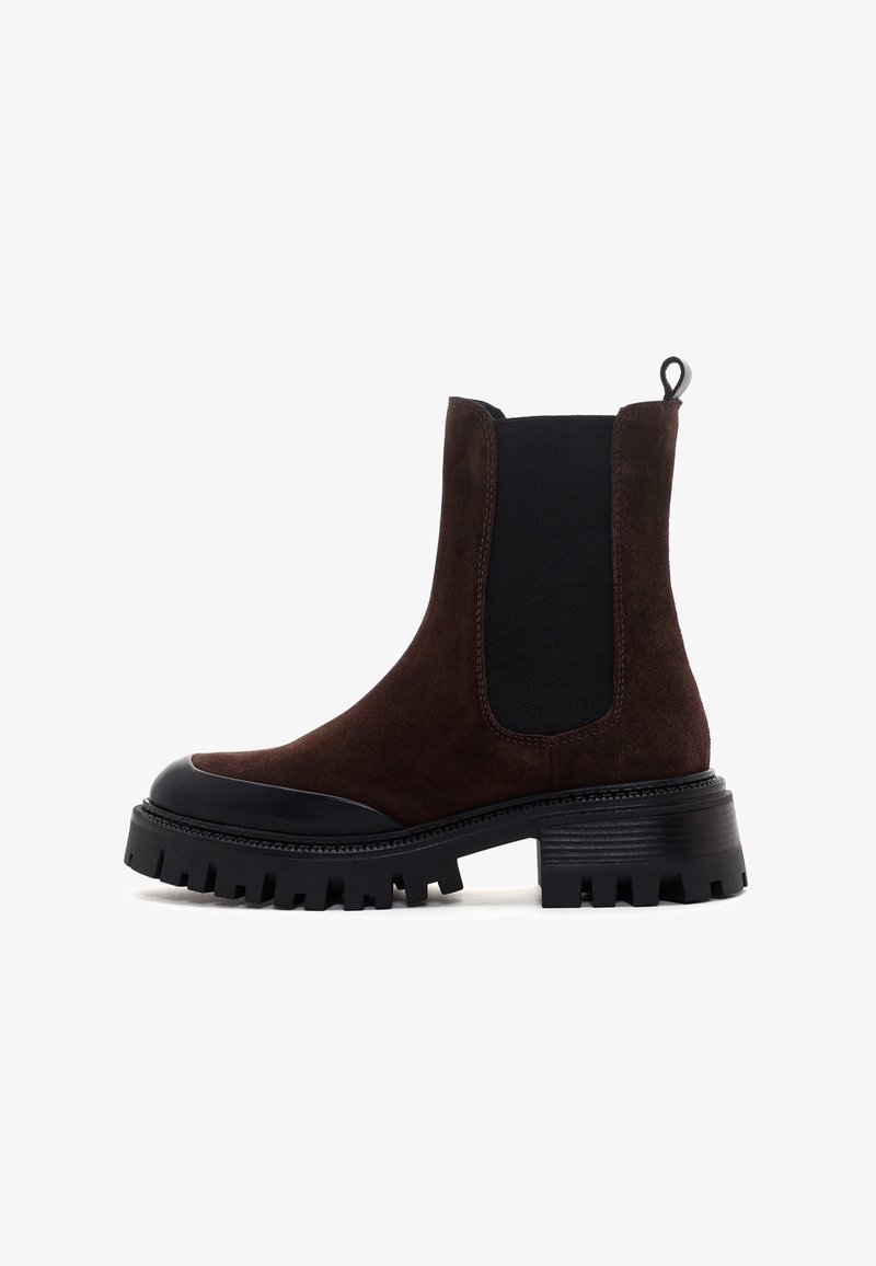 Bottes Chelsea en daim marron foncé avec panneau latéral élastique noir, semelle crantée épaisse noire et languette à l'arrière.