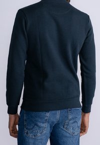 Sudadera azul marino de manga larga y cuello redondo, con una textura suave y un dobladillo acanalado, combinada con pantalones vaqueros.