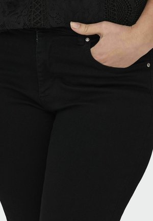 Højre hånd i frontlommen på sorte jeans båret med sort blonder top, viser øvre lår og taljeområde.