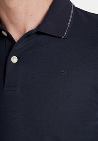 Granatowa koszulka polo wykonana z teksturowanej tkaniny, z dwoma guzikami, subtelnym logo i kontrastowym przeszyciem na kołnierzyku.
