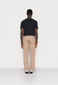 T-shirt noir à manches courtes, pantalon beige coupe droite, et chaussures noires avec semelles blanches. Design simple, sans motifs visibles.