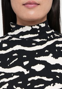 Fekete-fehér mintás garbó bordázott textúrával, absztrakt, hullámos vonalakkal, amelyek zebra csíkokra emlékeztetnek. Közeli kép.