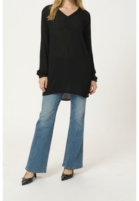 Tunique noire à manches longues avec un col en V, associée à un jean bleu évasé et des chaussures noires à bout pointu. Design simple avec un minimum de détails.