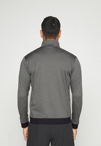 Chaqueta deportiva gris con un cuello alto, mangas largas y detalles negros en los hombros y los puños. Textura suave con un diseño ajustado.