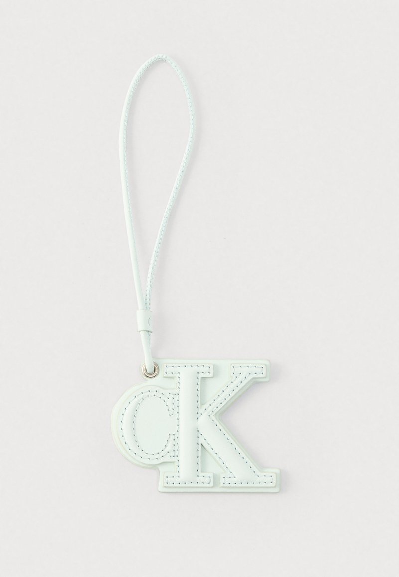 Porte-clés en cuir blanc avec les lettres "cK" cousues et une sangle bouclée pour attacher, sur un fond clair uni.