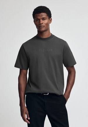 Donkergrijze katoenen t-shirt met een ronde hals en korte mouwen, voorzien van een subtiele reliëftext "POLO CLUB" op de voorkant.