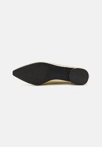 Zapato de tacón con punta afilada, parte superior texturizada en beige y suela de goma negra. Presenta un ligero brillo y está diseñado para ocasiones formales.