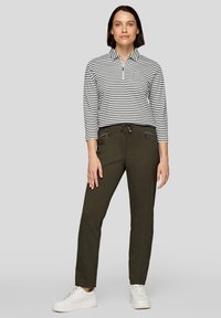 Gestreiftes Langarmshirt mit Viertelreißverschluss in Schwarz und Weiß, kombiniert mit olivgrünen Hosen mit Reißverschlusstaschen und weißen Turnschuhen.