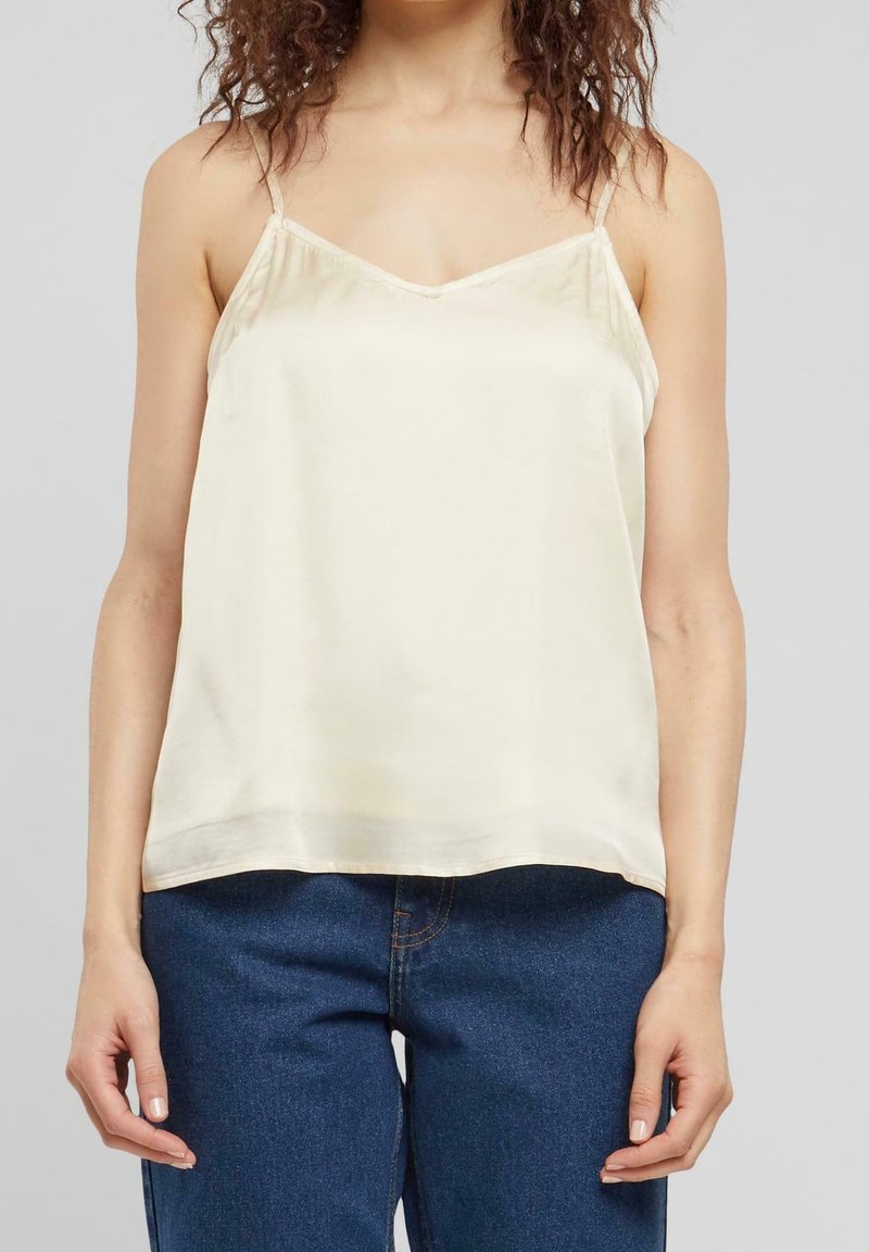 Cream satin camisole with thin adjustable straps, a V-neckline, and a relaxed fit, paired with dark blue denim jeans.