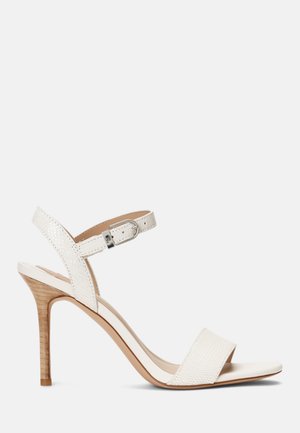 Sandale blanche à talon avec une bride texturée, une boucle à la cheville, un bout ouvert et un talon en bois. Design élégant avec des détails minimaux.