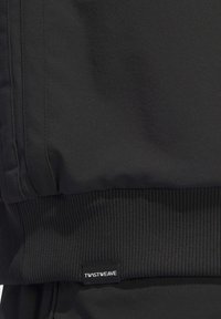 Černá bunda s hladkým materiálem a žebrovaným lemem. Výrazná značka "TWSTWEAVE" blízko spodní části. Jednoduchý design bez viditelných vzorů.