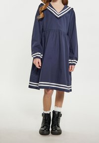 Tummansininen mekko, jossa on pitkät hihat, V-pääntie ja merimieskaulus, jossa on valkoiset raidat. Yhdistetty mustiin nauhakenkiin ja valkoisiin sukkiin.