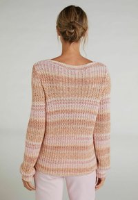 Donne con capelli castano chiaro raccolti in un bun, che indossa un maglione lavorato a maglia a righe rosa, beige e bianco e pantaloni rosa pallido, di spalle rispetto alla fotocamera.