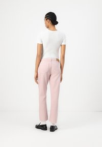 Jeans rosa chiaro con design a gamba dritta, dotati di tasche posteriori e orlo grezzo. Abbinati a una maglietta bianca a coste attillata e scarpe nere.