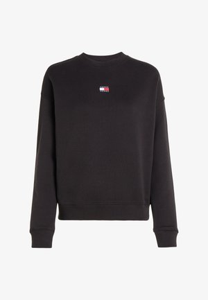 Mustra must hoon täiesti musta dressipluusi, millel on soonikuline ümar kaelus ja pikad varrukad. Rinna peal on väike logopatch punases, valges ja sinises värvitoonis.