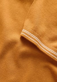 Gros plan d'un tissu tricoté jaune moutarde avec un revers plié comportant deux fines bandes blanches horizontales.