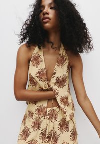 Béžový halter top s hlubokým V-výstřihem, zdobený hnědými květinovými vzory, spárovaný s odpovídajícími kalhoty s elastickým pasem na šňůrku.