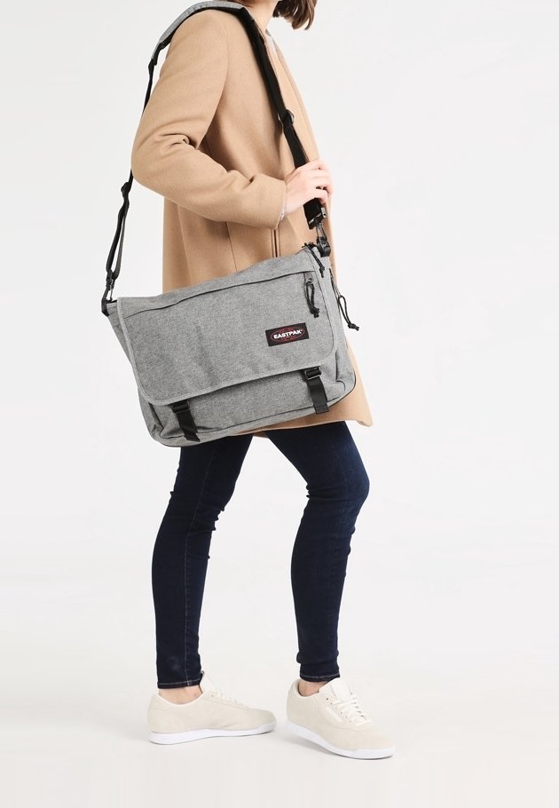 Borsa a tracolla grigia con chiusura a pattina, tracolla regolabile e accenti neri. Il materiale appare strutturato, adatto all'uso quotidiano.