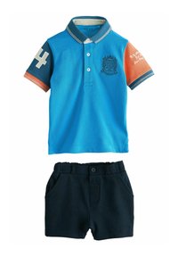 Blå pikétröja med kontrasterande orange ärm, nummer "4" och emblemdetalj. Kombinerad med mörkblå shorts med sidfickor.