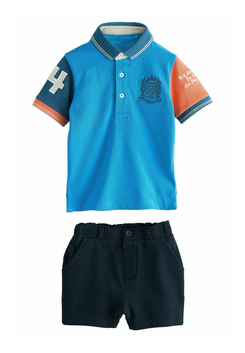 Blå pikétröja med kontrasterande orange ärm, nummer "4" och emblemdetalj. Kombinerad med mörkblå shorts med sidfickor.
