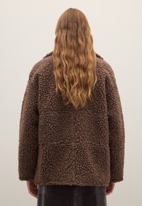 Veste en polaire marron à surface texturée et duveteuse. Coupe ample, forme carrée, épaules tombantes. Vue arrière présentant des détails minimaux.