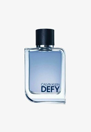 Klar glasflaske med afrundede kanter, fyldt med lys blå væske, toppet med en struktureret sort kork. "CALVIN KLEIN DEFY" trykt i mørkeblåt.