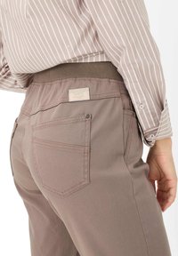 Pantaloni marrone chiaro con vita elasticizzata, dotati di due tasche posteriori e un'etichetta in vita, abbinati a una camicia a righe.
