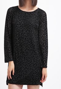 Svart leopardmönstrad klänning med långa ärmar, rund hals och ett mjukt, strukturerat tyg med en subtil lyster. Sidoklipp i fållen.