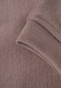 Gros plan d'un tissu tricoté mauve replié mettant en valeur la texture et les coutures détaillées.