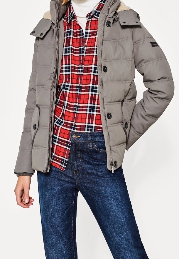 Grå polstret jakke med hætte, der har en fleecekrave, knaplukning og sidelommer, båret over en rød- og sortternet skjorte og blå jeans.