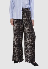 Leopardprint wijde pijpen broek met een zwart en beige kleurenschema; elastische tailleband en zachte stof; gecombineerd met een lichtblauw gestreept shirt.