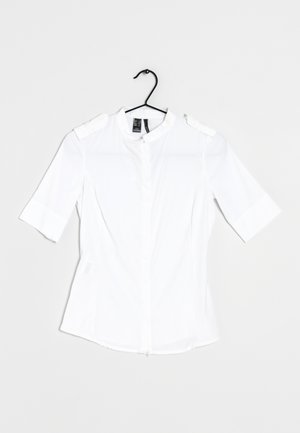 Hvid kortærmet bluse med høj krave, knaplukning foran og skulderdetaljer. Glat stof uden mønstre, minimalistisk design.