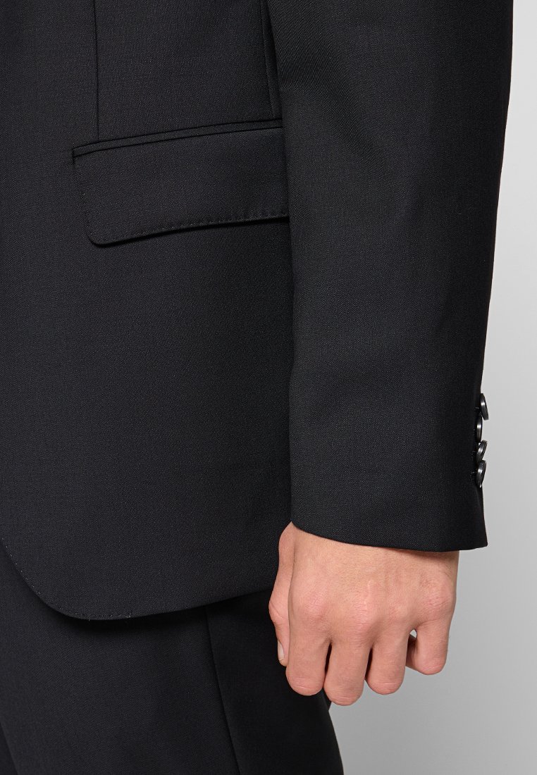 Close-up van de rechterhand van een persoon naast de manchet en de zijklep van een zwart colbert.